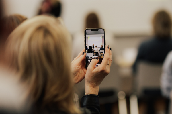 Beim FEMALE FOUNDERS CUP 2025 in der IHK Reutlingen macht eine Besucherin ein Foto von der Bühne mit ihrem Smartphone. Bildrechte: Maik Jarek Photography.