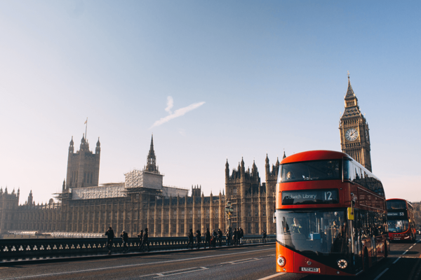 Fotoaufnahme von einem roten Doppeldeckerbus vor dem Palace of Westminster und dem Elizabeth Tower im Hintergrund.