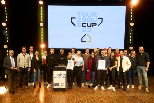 Gruppenbild der Teilnehmenden des Gründungswettbewerbs Start-up BW Elevator Pitch Tourismus Cup 2023 auf einer Bühne mit Staatssekretär Dr. Patrick Rapp.