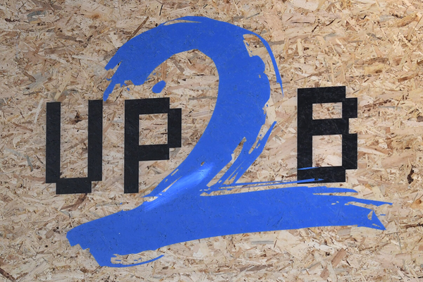 Logo des Up2B Accelerators auf einer Holzplatte - schwarze Buchstaben, blaue Zahl zwei