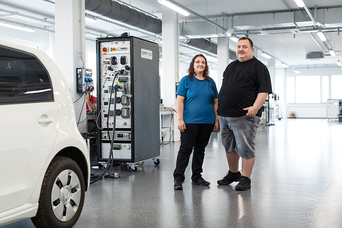 Gründungsteam der comemso gmbh (eine Frau, ein Mann) in einer Werkstatthalle mit einem Fahrzeug und Messinstrumenten.