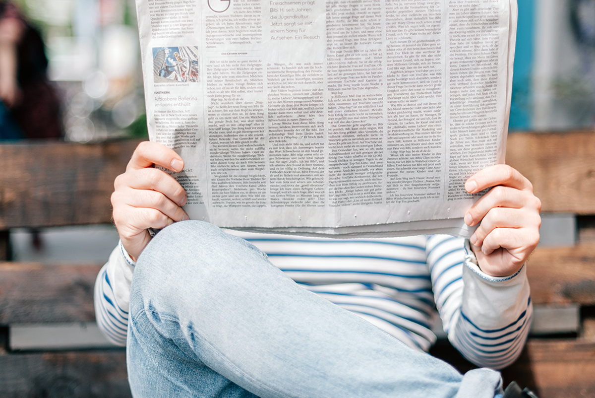 Ein Mann sitzt auf einer Parkbank und liest eine Tageszeitung.