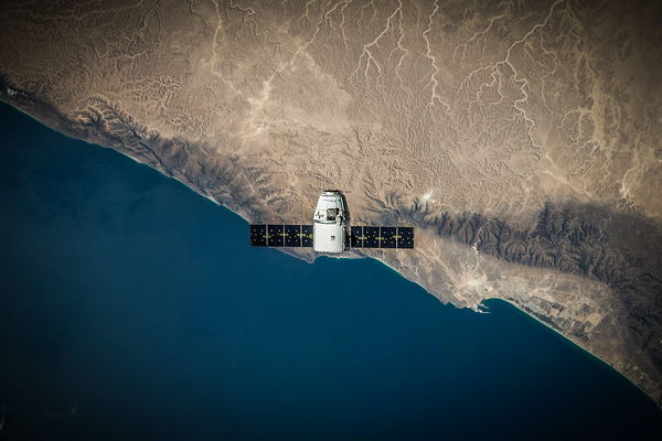 Ein Satellit schwebt in der Luft über eine Küste.