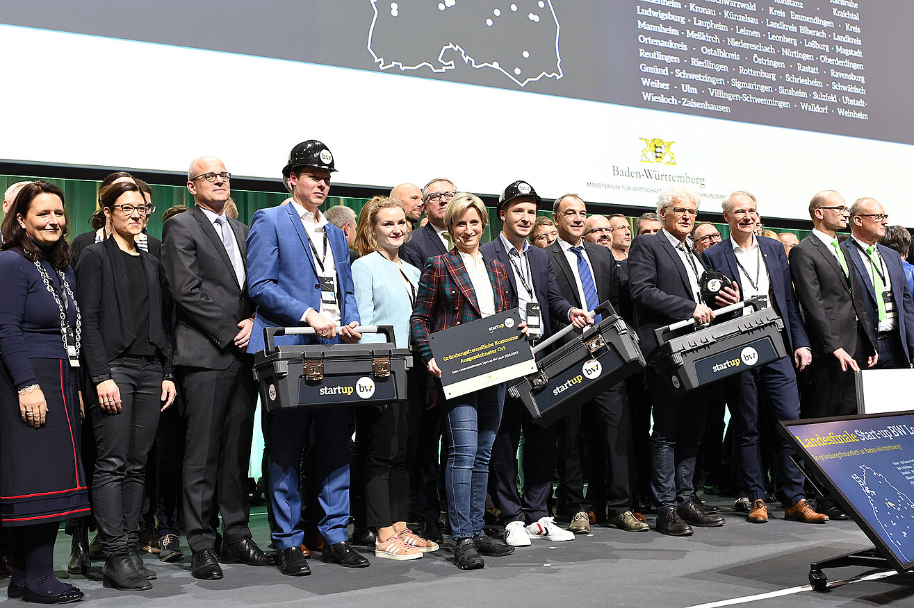 Beim Start-up BW Local Finale stehen alle Teilnehmenden gemeinsam auf der Bühne. Wirtschaftsministerin Dr. Hoffmeister-Kraus hält die Auszeichnung in den Händen.