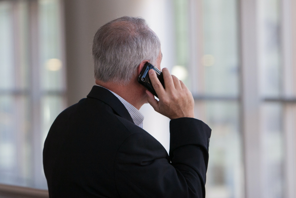 Älterer Mann im schwarzen Anzug telefoniert mit seinem Smartphone.