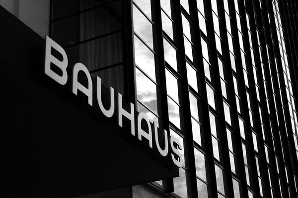 Schwarz-weiß Aufnahme von einem Gebäude im Bauhausstil. Am Eingang formen angebrachte Buchstaben das Wort "Bauhaus".