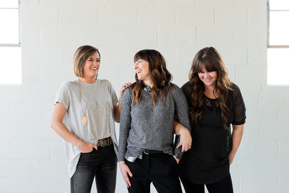 Drei Unternehmerinnen stehen nebeneinander vor einer weißen Wand.