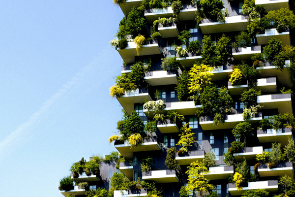 Hochhaus mit zahlreichen Balkonen, die dicht mit grünen Pflanzen und Bäumen bepflanzt sind. Die Vegetation bedeckt große Teile der Fassade.
