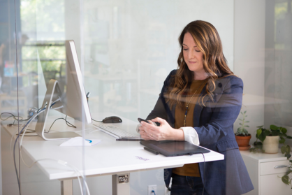 Eine Unternehmerin steht an einem höhenverstellbaren Schreibtisch in einem Büro.