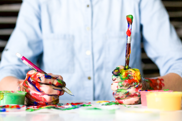 Farbverschmierte Hände mit Pinsel und Stift.