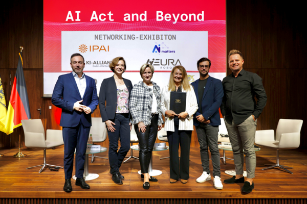 Aufnahme im Rahmen der Diskussionsrunde “AI Act and beyond” in Brüssel bei der Übergabe des Forderungskatalogs. Wirtschaftsministerin Dr. Nicole Hoffmeister-Kraut, Lucilla Sioli und weiteren Teilnehmenden der Diskussionsrunde stehen im Halbkreis auf einer Bühne. Bild: Cédric Puisney Photography.