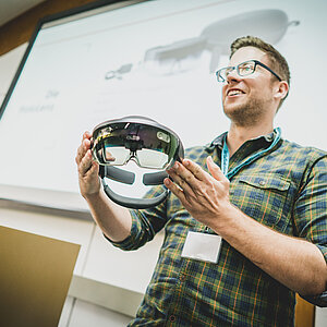 Ein Mann hält einen Vortrag und zeigt dem Publikum eine innovative VR-Brille.