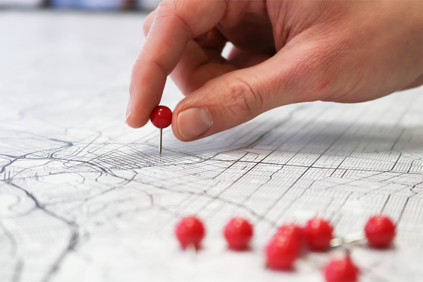 Auf einem ausgedruckten Stadtplan werden rote Stecknadeln von einer Hand platziert.