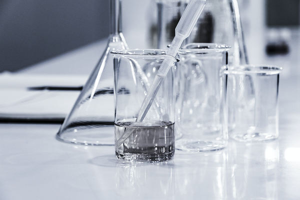 Vier Labor-Gläser in verschiedenen Größen stehen nebeneinander. In einem Glas befindet sich eine chemische Flüssigkeit und eine Pipette.