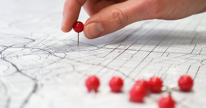 Eine Hand platziert rote Stecknadeln auf einem ausgedruckten Stadtplan.