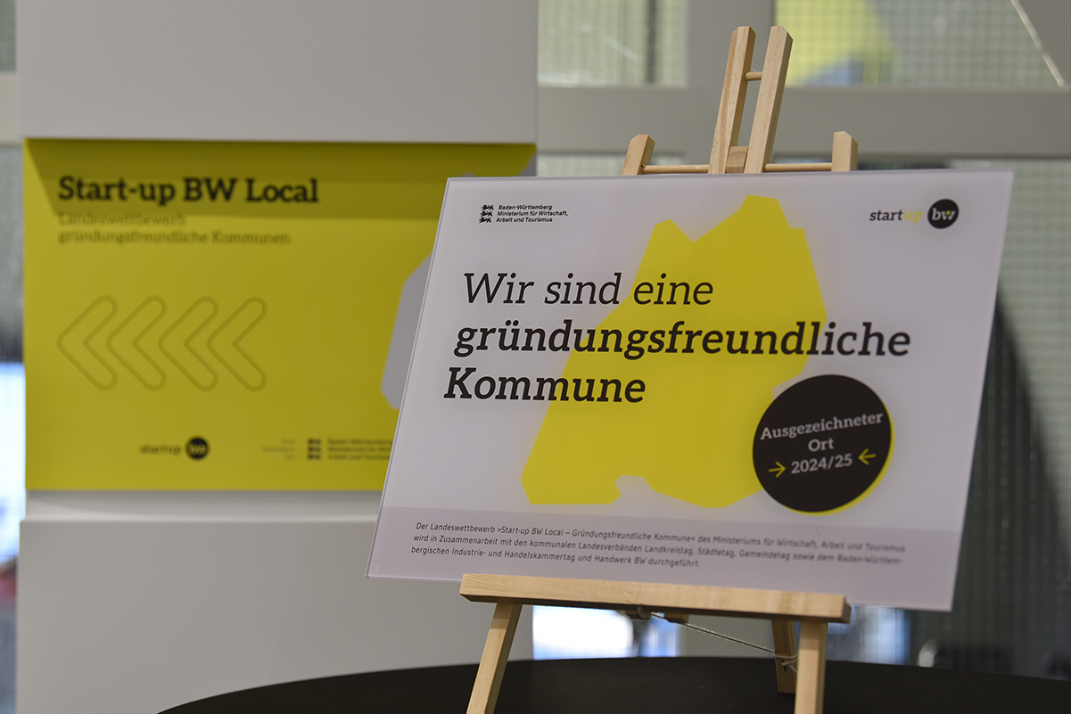 Hinweistafel auf einem Aufsteller mit dem Text: Wir sind eine gründungsfreundliche Kommune, Ausgezeichneter Ort 2024/2025. Logos Start-up BW sowie die drei Landeslöwen für das Ministerium für Wirtschaft, Arbeit und Tourismus Baden-Württemberg.