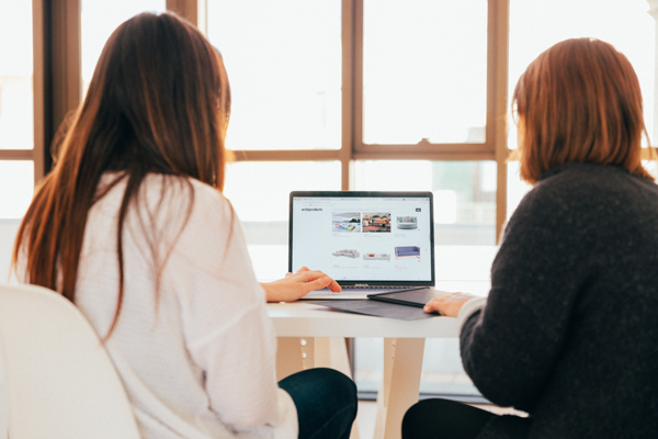 Zwei Frauen sitzen mit dem Rücken zur Kamera und arbeiten zusammen an einem Laptop.