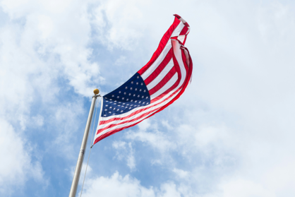 Die Flagge der Vereinigten Staaten weht an einem Fahnenmast vor leicht bewölktem Himmel.