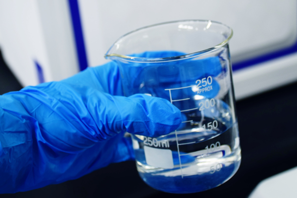 Hand in blauem Gummihandschuh mit Laborgefäß und Flüssigkeit.
